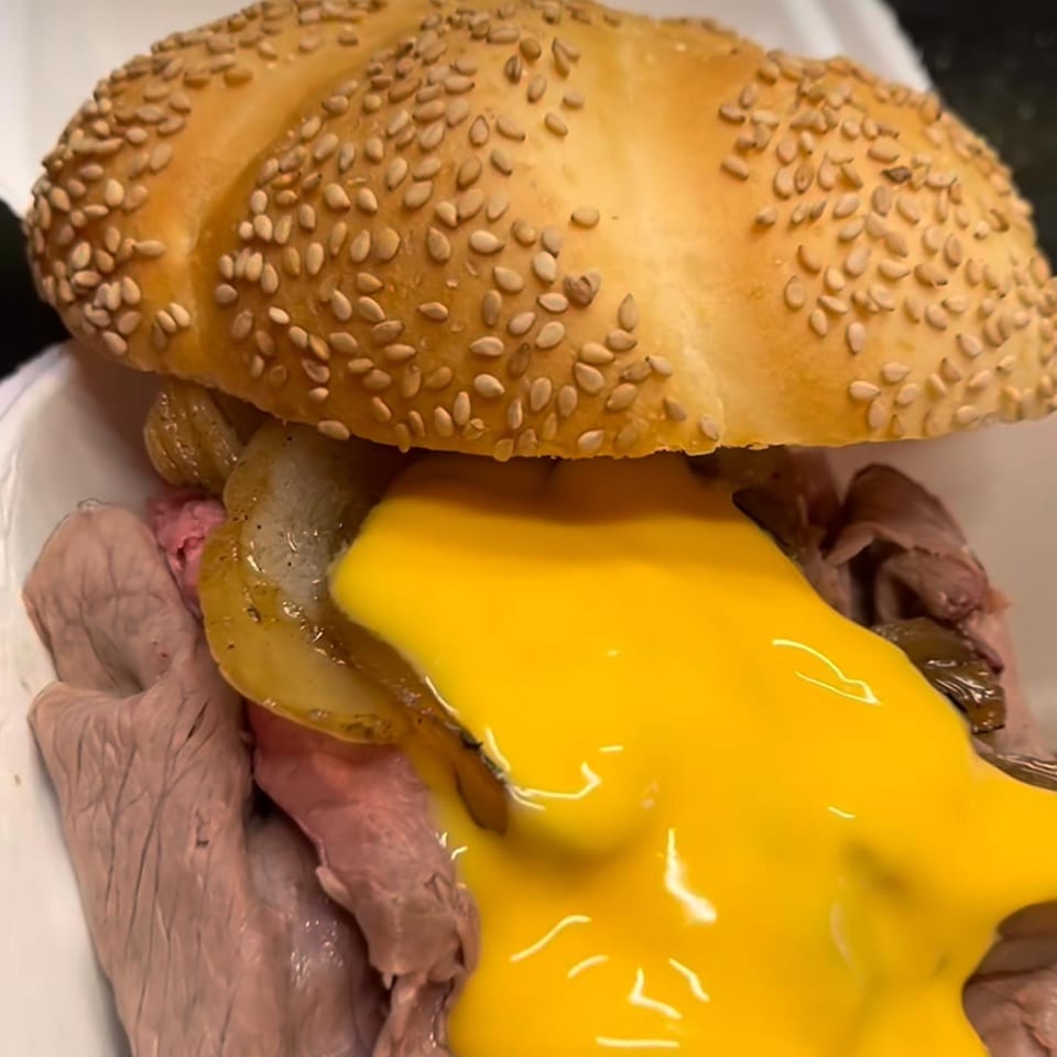 A close-up of an On a Roll roast beef sandwich with melted cheese and grilled onions.