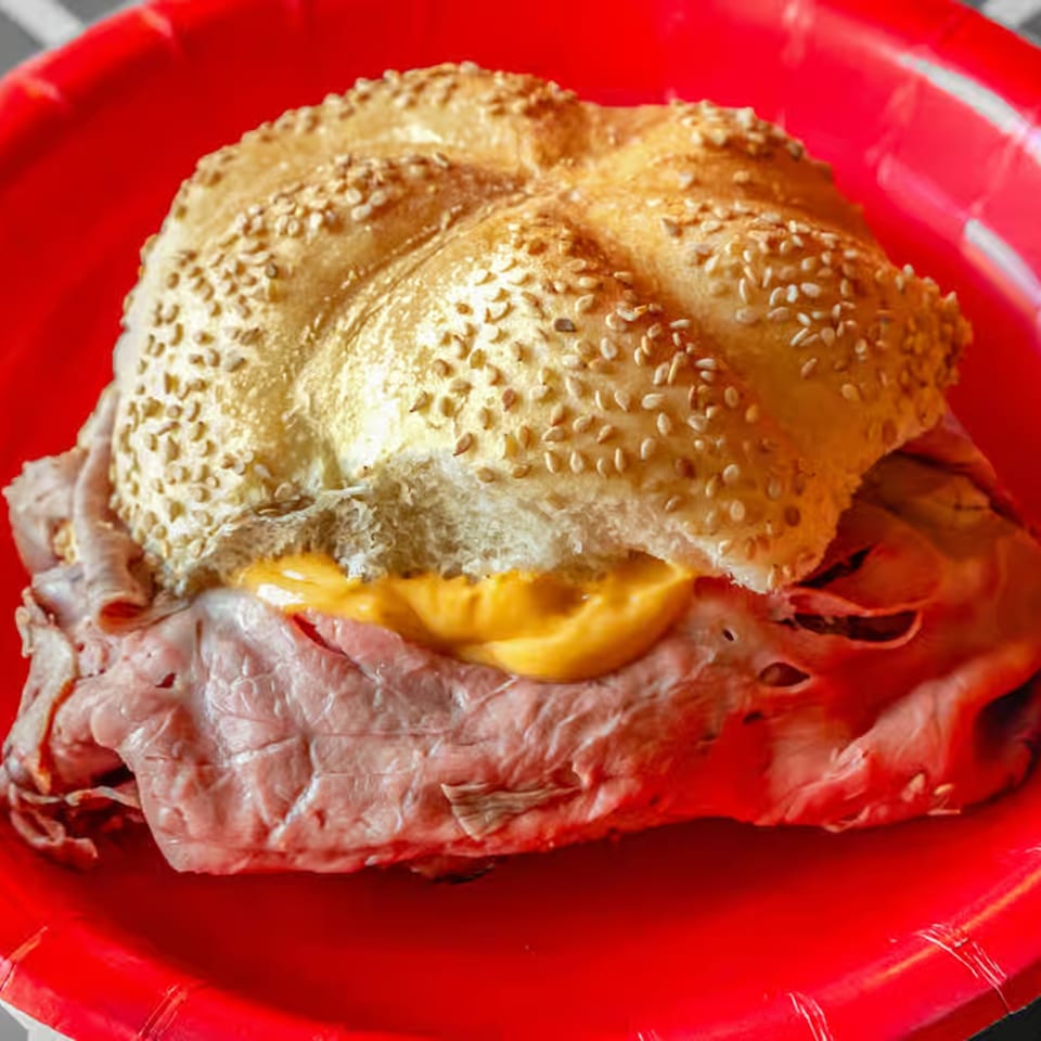 On a Roll's roast beef sandwich with cheese on a sesame seed bun, served on a red plate.