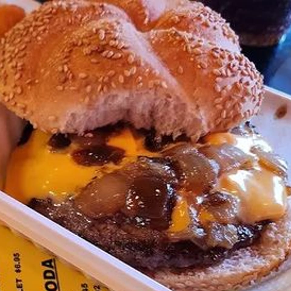 Close-up of an On a Roll burger with melted cheese and caramelized onions on a sesame seed bun.