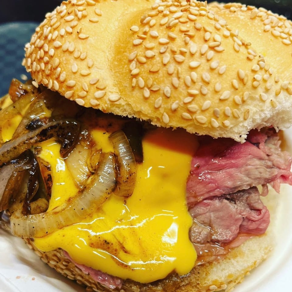 Close-up of an On a Roll burger with melted cheese, caramelized onions, and rare beef.